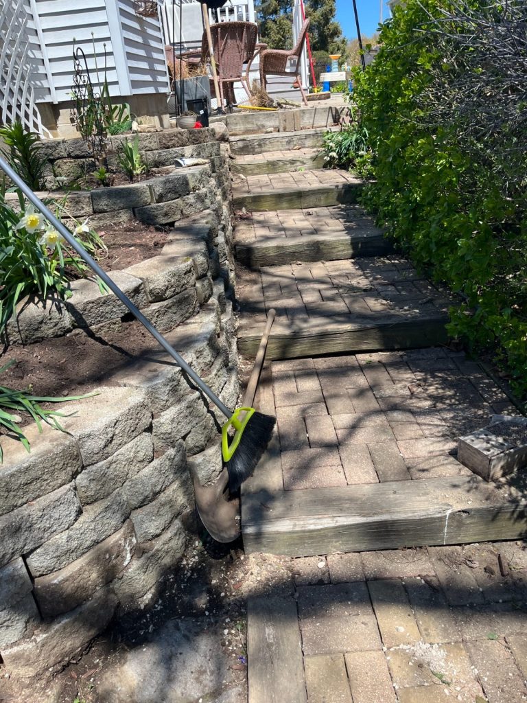 Completed garden retaining wall and leveled brick pathway, with restored stone alignment and tidy garden edging.