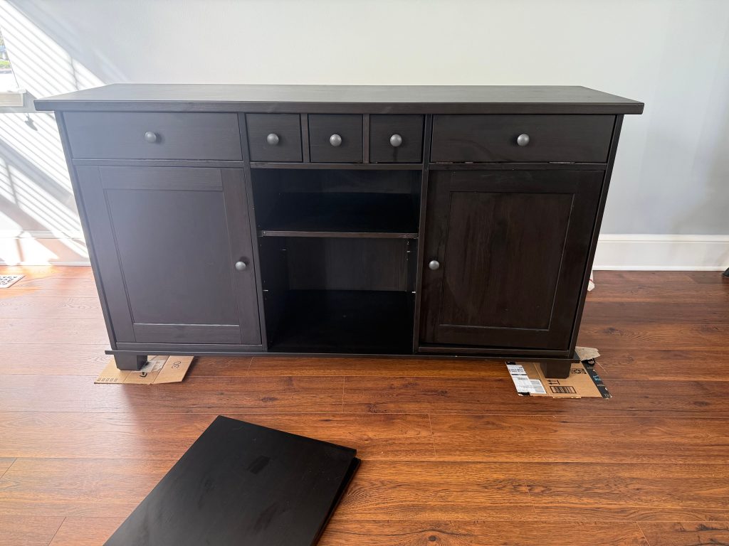 Dark wooden sideboard before refinishing, with cabinet doors and drawers in original condition on a hardwood floor.